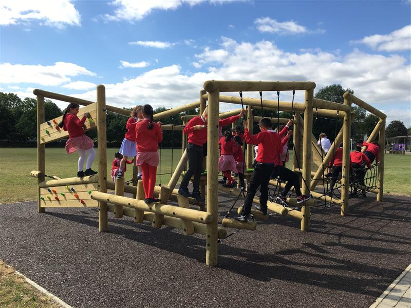 children in red school uniform clib around one of our forest climbing trim trails in the sunshine with safety surfacing beneath