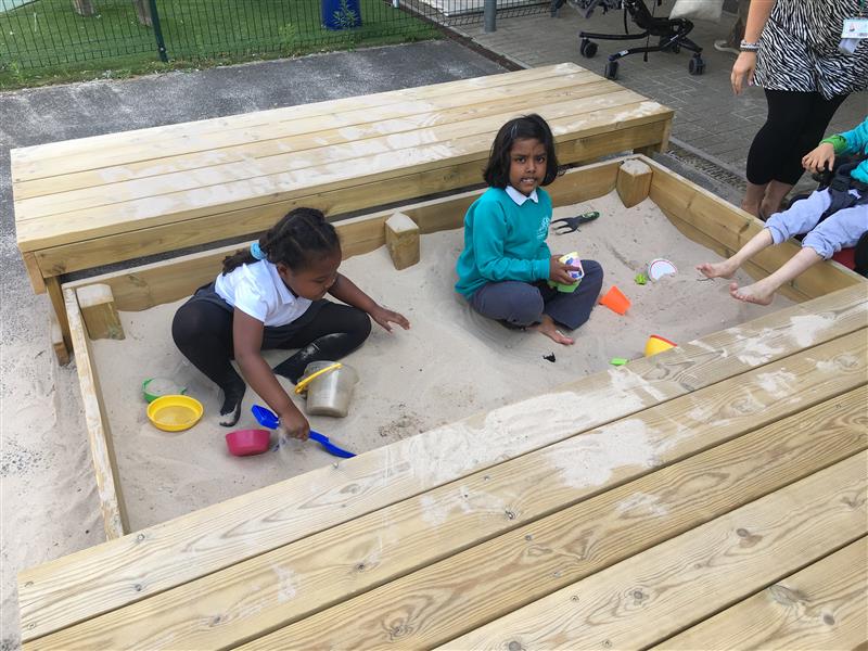 children sit in the sand pit and play with toys in the sand