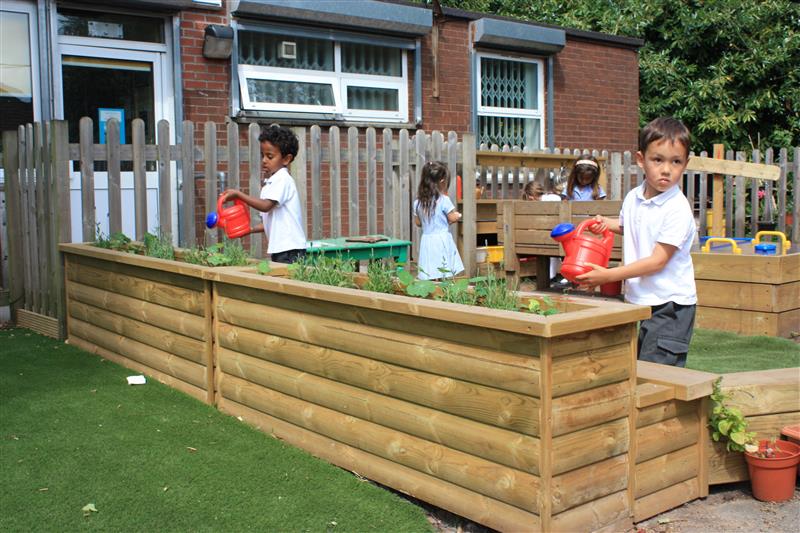 children stand around the planters and water them with their red watering cans 