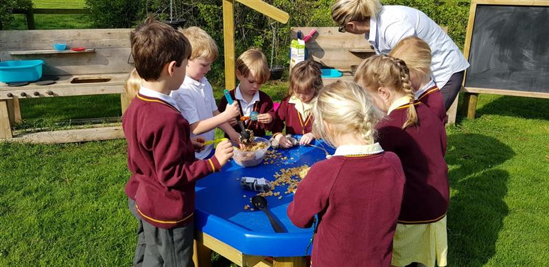 children in burgundy school uniform and a teacher gather around a tuff spot table and play with cheerios