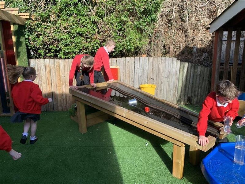 children in red school uniform playing with the timber damming station