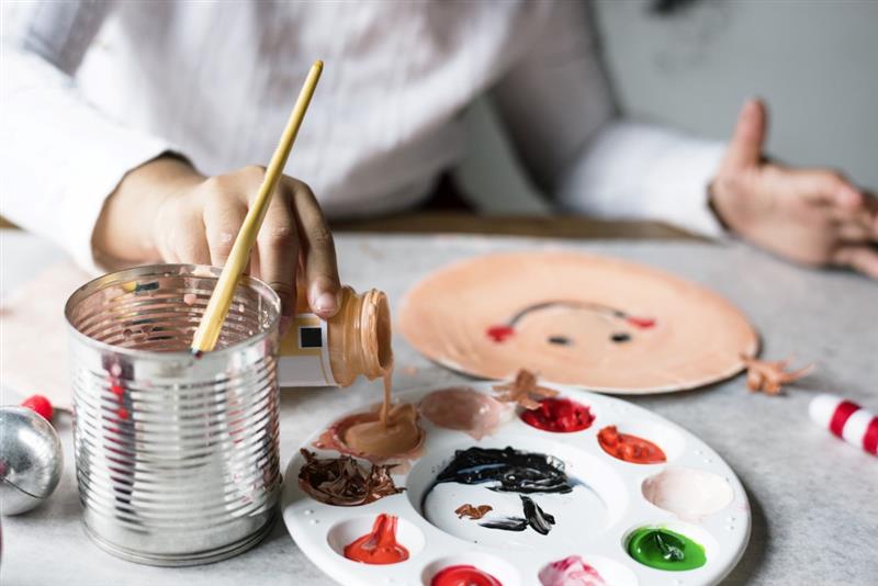 a child paints a paper plate with acrylic paint and a wooden paint brush