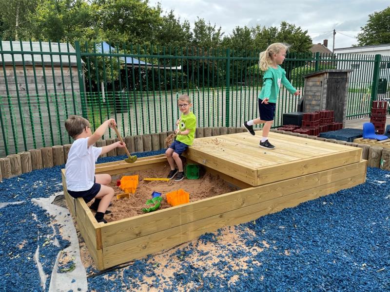 three children play in the sliding sandpit with the sand, digging, making sandcastles and running around