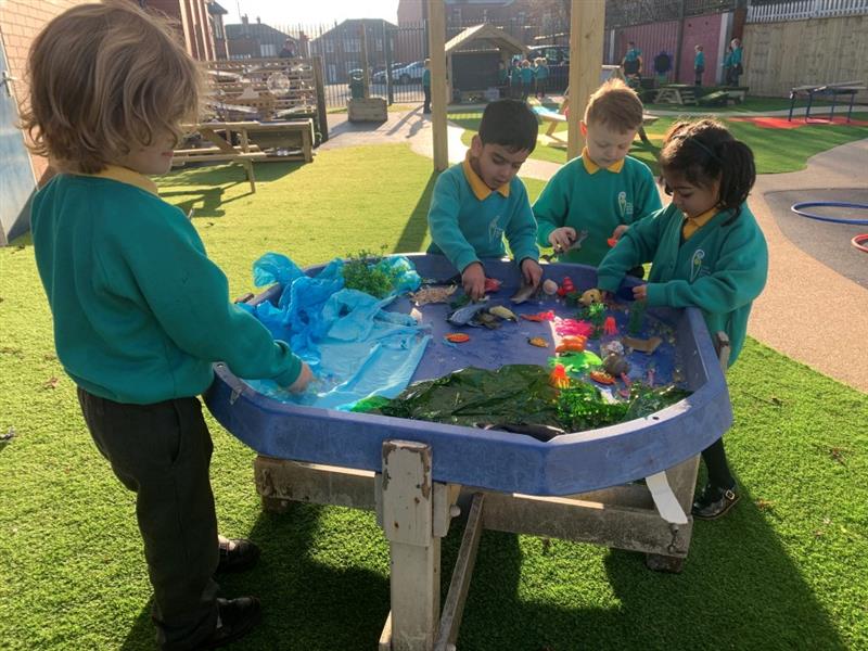 children gather around the tuff spot table and play with toy dinosaurs and messy play items
