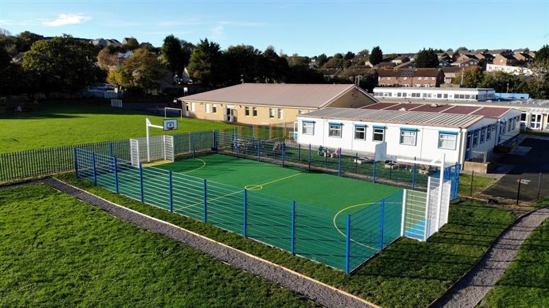 a distanced view of the muga in the playground with the goal posts and basketball posts