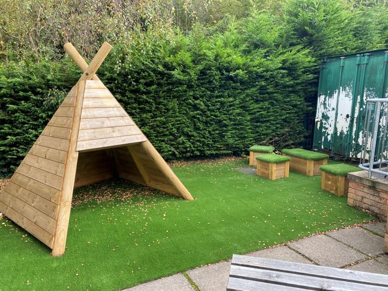 another side view of te timber wigwams and the artificial grass topped seats with artificial grass surfacing below