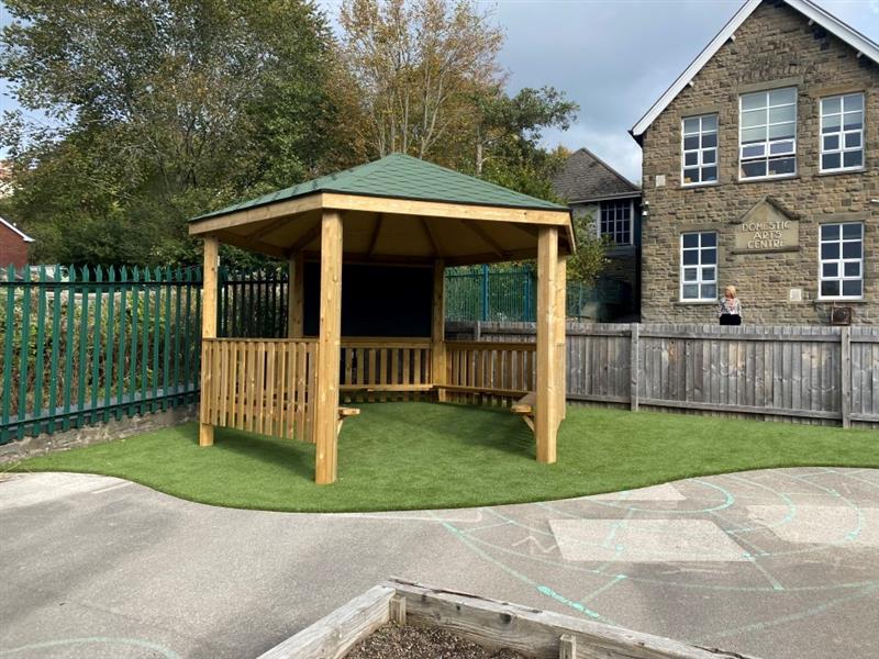 an outdoor classroom on artificial grass surfacing with the stone school in the background