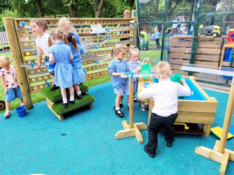 children in blue and white school uniform play with the water wall and the water table that comes included in the water play package
