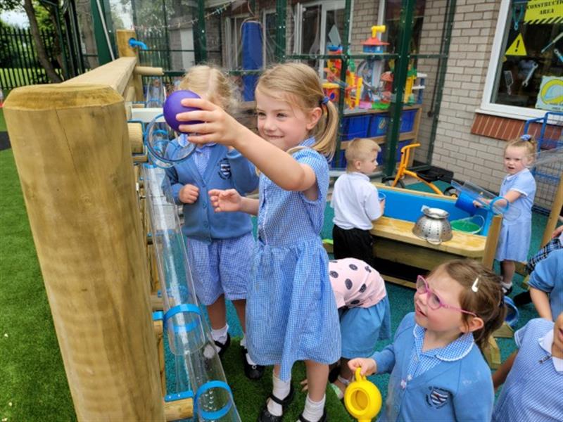 children in blue and white school uniform drop a purple ball down the water wall and watch as it falls