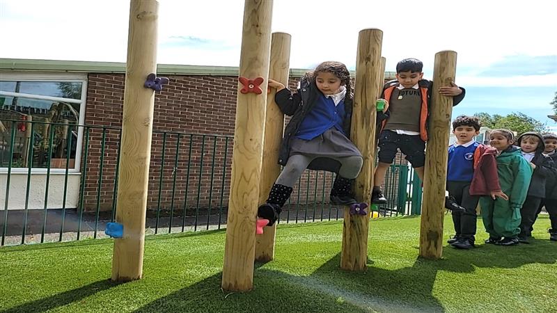 children cross the climbing poles with artificial grass surfacing underneath