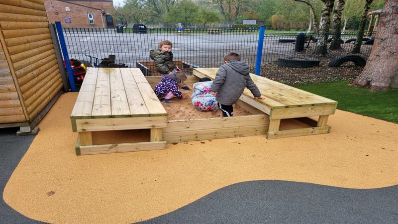 four children sat in the sand box with lid in winter coats and play with the sand 