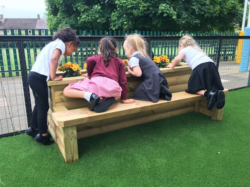 children kneel on the side of the planter bench and look into the planter