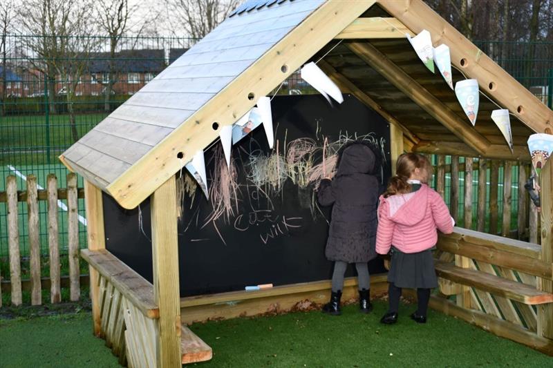 two little girls stand and draw on the back board of the playhouse