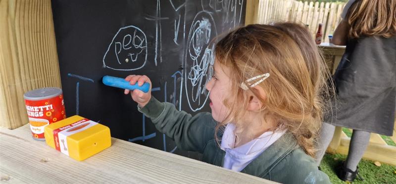 a little girl stands at the chalkboard and scribbles on the board