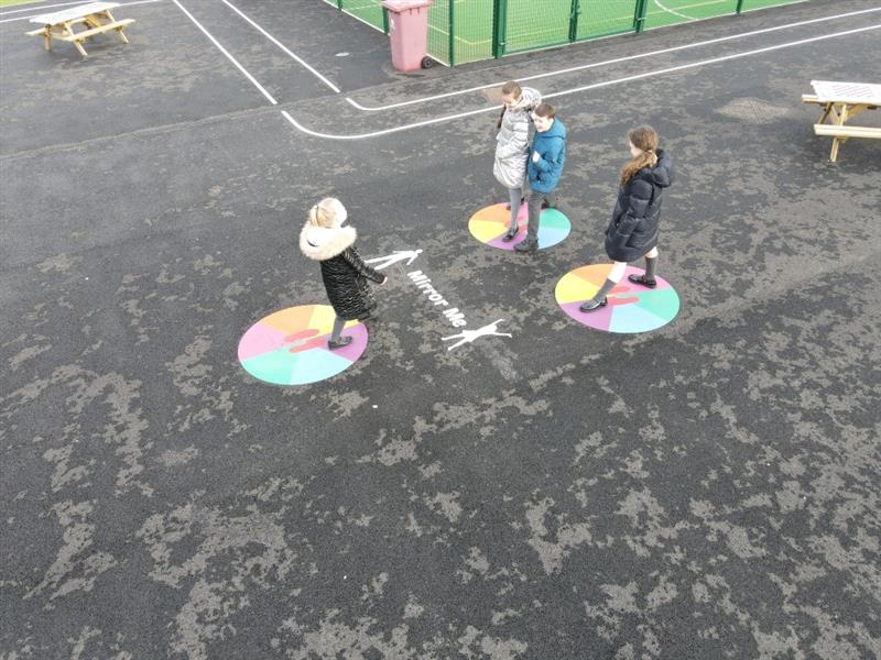 children stand on the mirror me playground markings mimicking each others behaviour and movements 