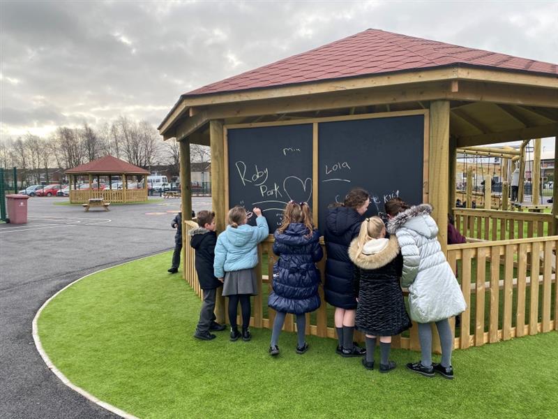 children stand around the back of the hexagonal gazebo and draw on the chalkboard 