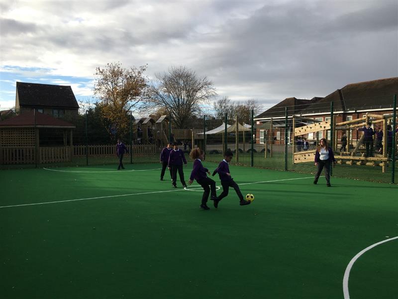 6 children playing football on a muga pitch installed onto the school playground