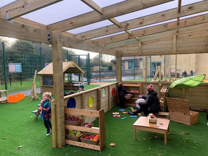 the inside of the timber canopy, with artificial grass surfacing filled with toys, tables and resources