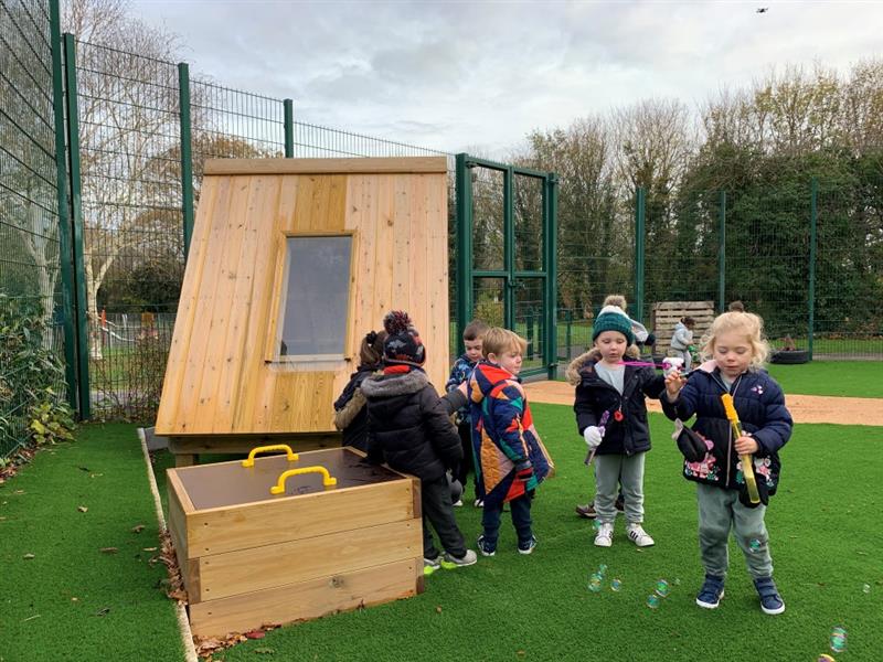 children stand in front of the mud box on the artificial grass playturf and play with bubbles