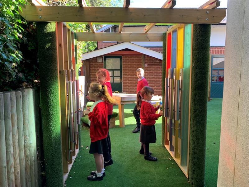 four children stand under the rainbow sensory tunnel and play with the sensory panels inside