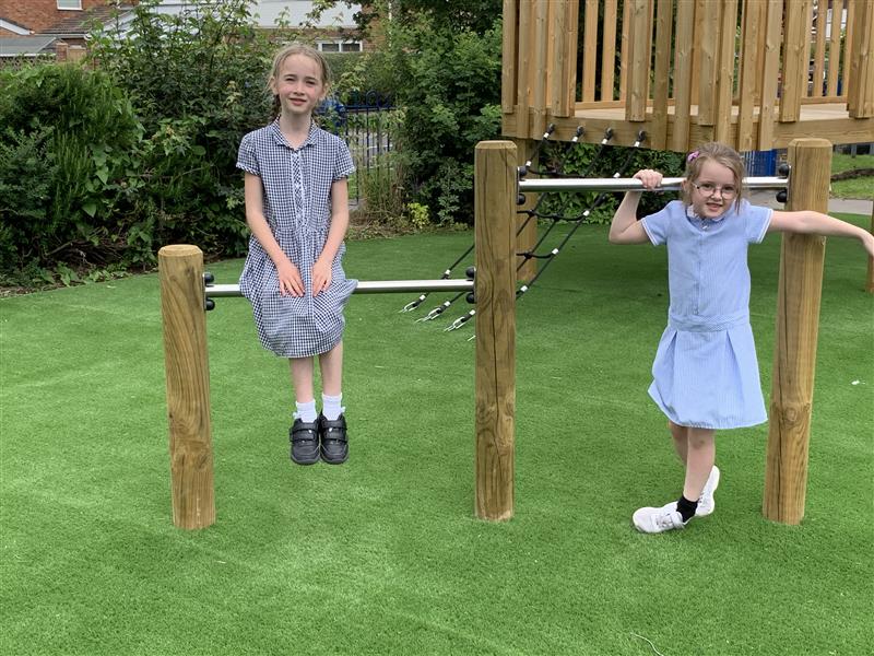 two little girls in blue school uniform swinging on metal poles held up by timber frames