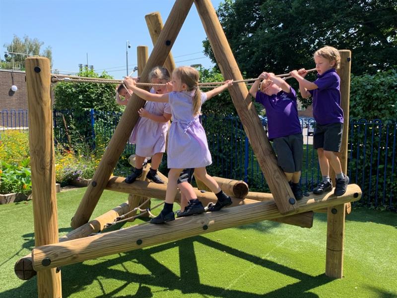 children in purple school uniform clamber across a timber wall climbing frame