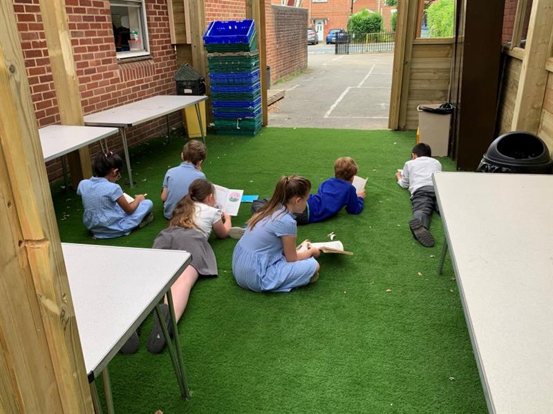 children laying on the artificial grass surfacing within the outdoor classroom