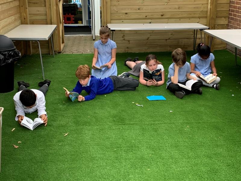 children reading in the outdoor classroom whilst lying down on the artificial grass