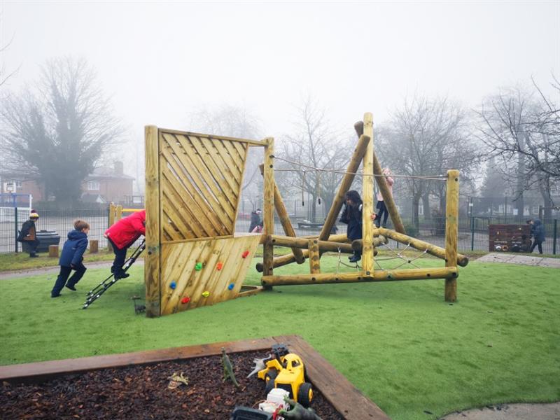 Two children climbing and swinging on the ropes of a log and rope climbing frame and a child climbing up the climbing net onto the climbing frame platform