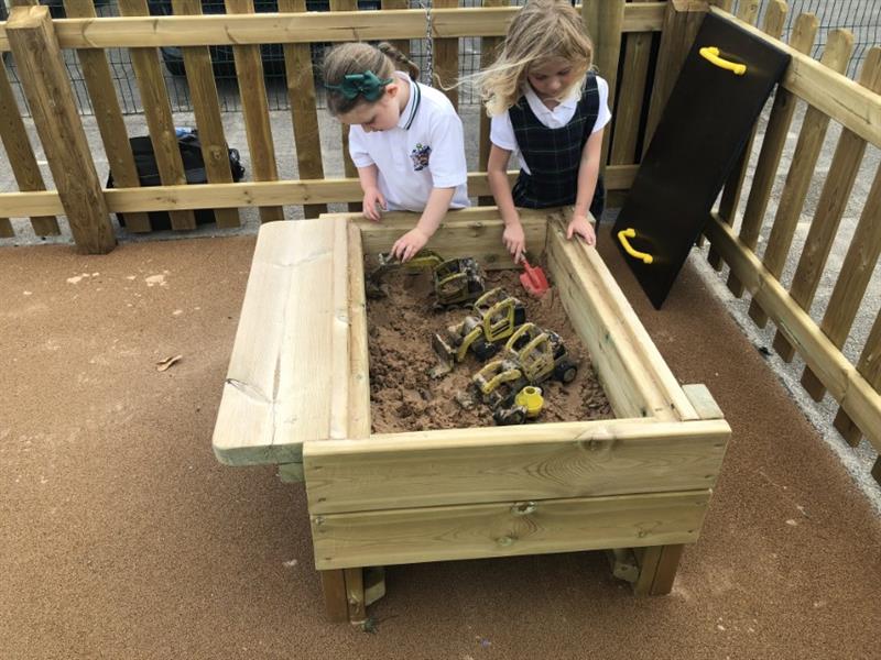 Two children playing with 4 toy diggers and spades in Pentagon Play's sand table