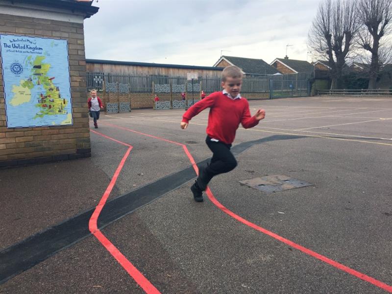 Two children in red school jumpers running their daily mile using red line playground markings as a route