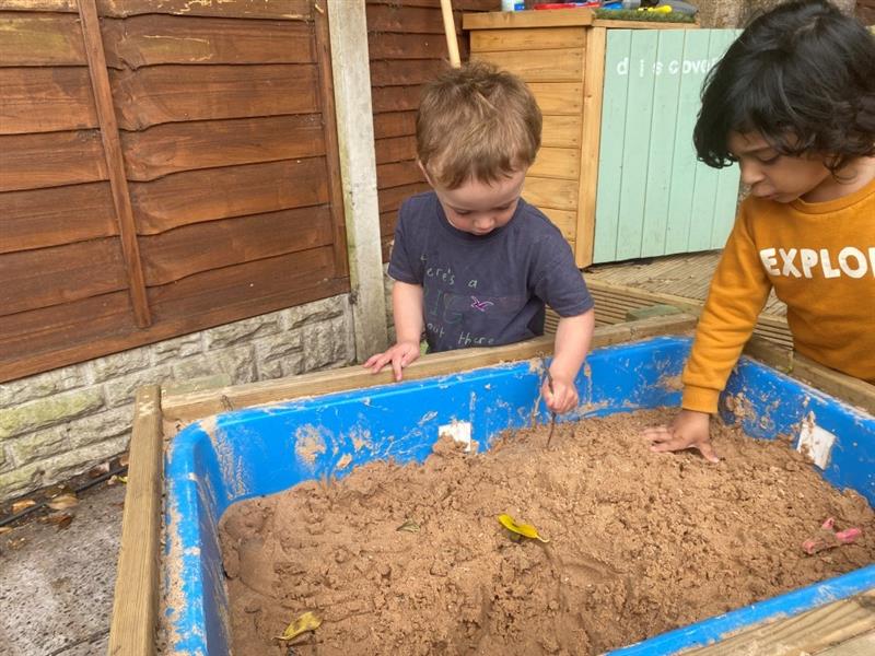 two little boys playing with the sand in the sand table with lid