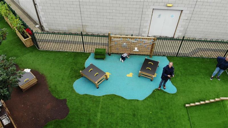 A birds eye view of the water wall, there are 2 messy play tables on top of the bespoke wetpour design, there are 2 ducks within this design. 