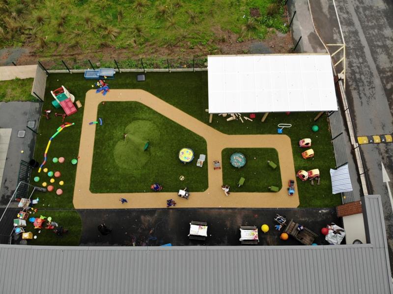 a birdseye view of the remodel showing the top of the canopy and the green artificial grass surfacing, the beige wetpour can be seen and there is lots of toys laying about on the floor