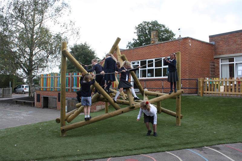 children in blue and white school uniform play on the timber bowfell climbing frame with green artificial grass playturf beneath it