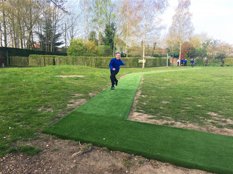 A child running around an artificial grass daily mile track installed onto their school field