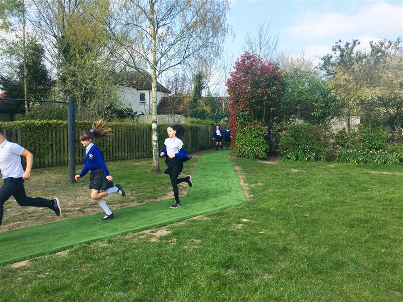 5 children running around an artificial grass daily mile track installed onto the school field
