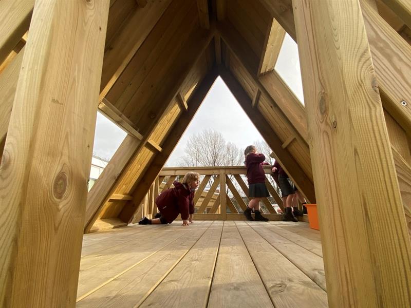 children stand in the learning den and look over the timber balcony down to the playground below