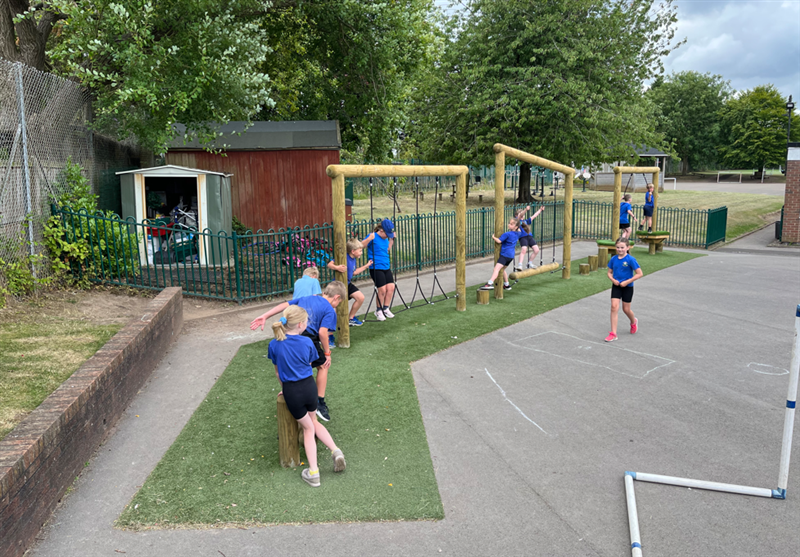 A birds eye view of the ks1 trim trail in a school playground, a class of children are climbing on it