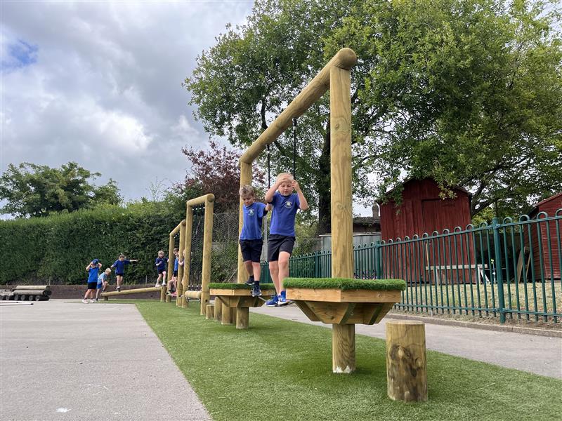 A low angle of a class of children playing on the trim trail in their playground