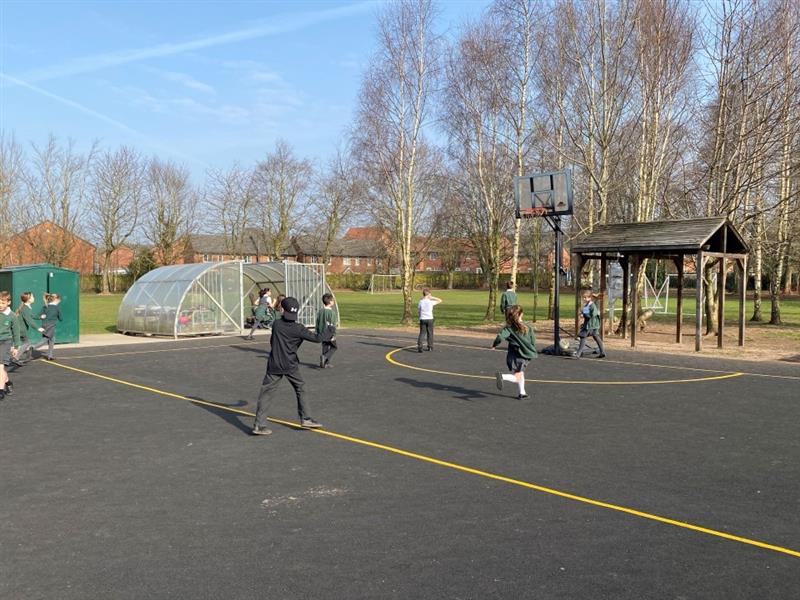children aim for the hoop on the netball court made of wetpour