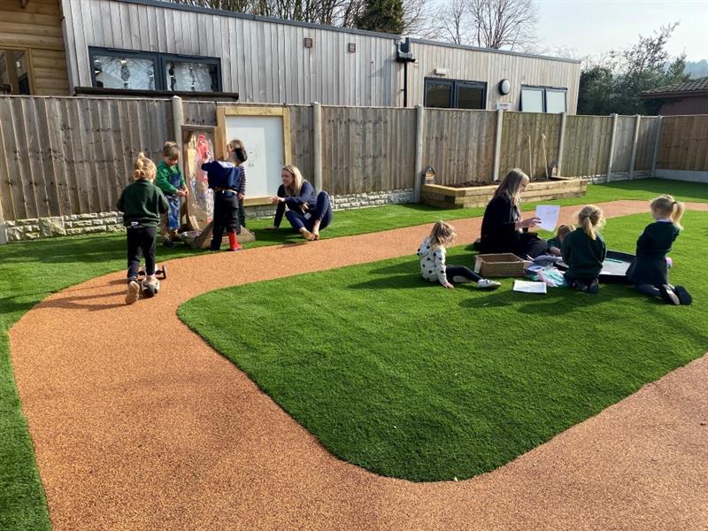 children sit on the artificial grass being read to by a teacher
