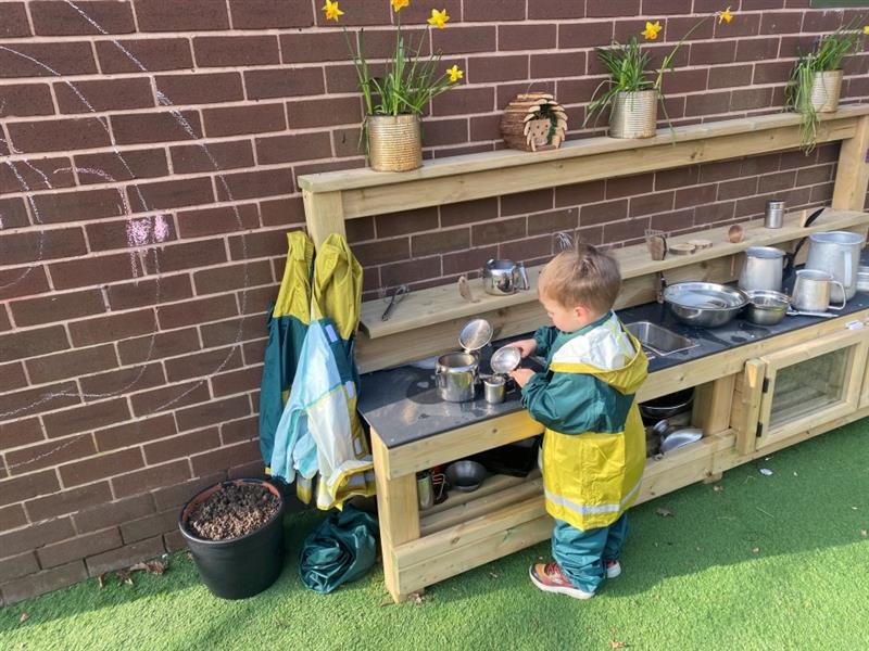 a child stands at the mud kitchen and pretends to cook in the mud kitchen