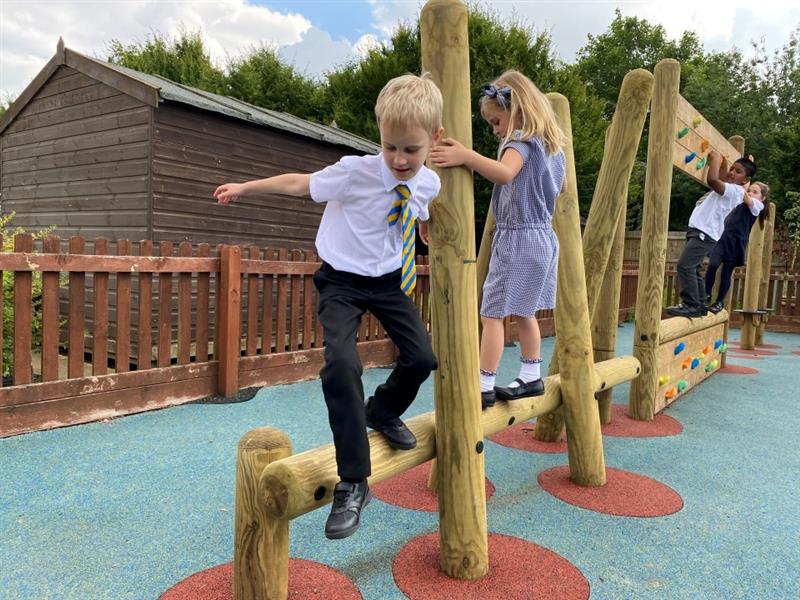 a little boy in black pants, white shirt and a yellow and navy striped tie leaps down from the timber log weaver onto the blue wetpour