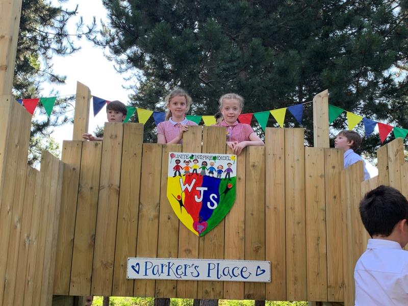 Children standing near sign decorated like a rainbow coat of arms reading parkers place