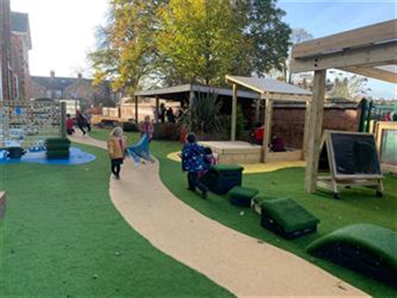children playing on their new eyfs playground development, a long brown wetpour strip is running through the inside of the playground.
