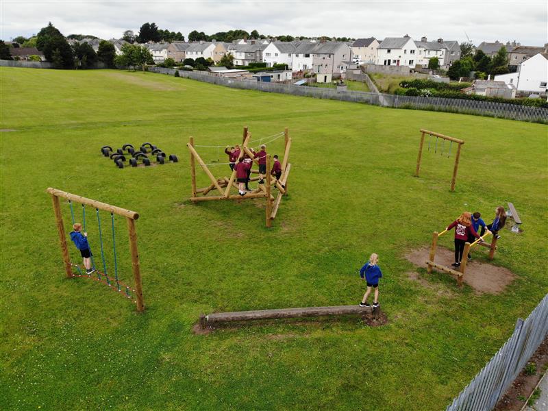 A birds eye view of the ks2 trim trail with the bowfell climbing frame in the middle of it, there are 9 children playing around the different pieces of equipment.