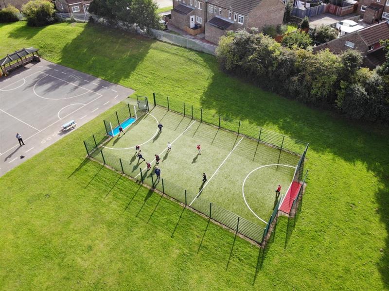 a birdseye view of the MUGA pitch being played on by pupils with one side a red team and one side a blue team