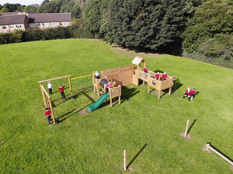 children play on the framlingham timber play tower on natural grass in red school uniforms