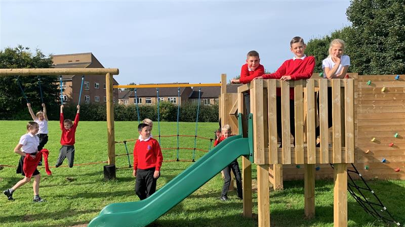 children in red, white and black uniform stand on top of the play tower and look at the camera